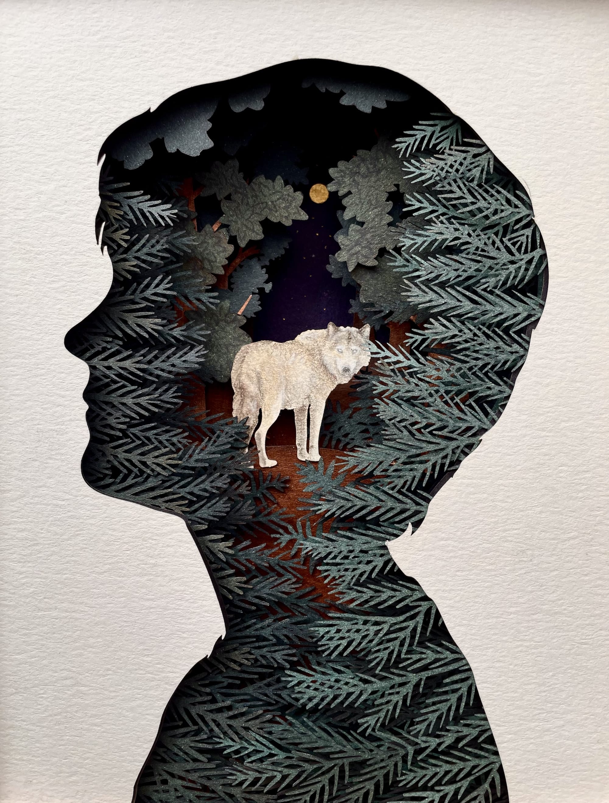 a paper collage of a wolf amid a forest inside the silhouette of a person in profile