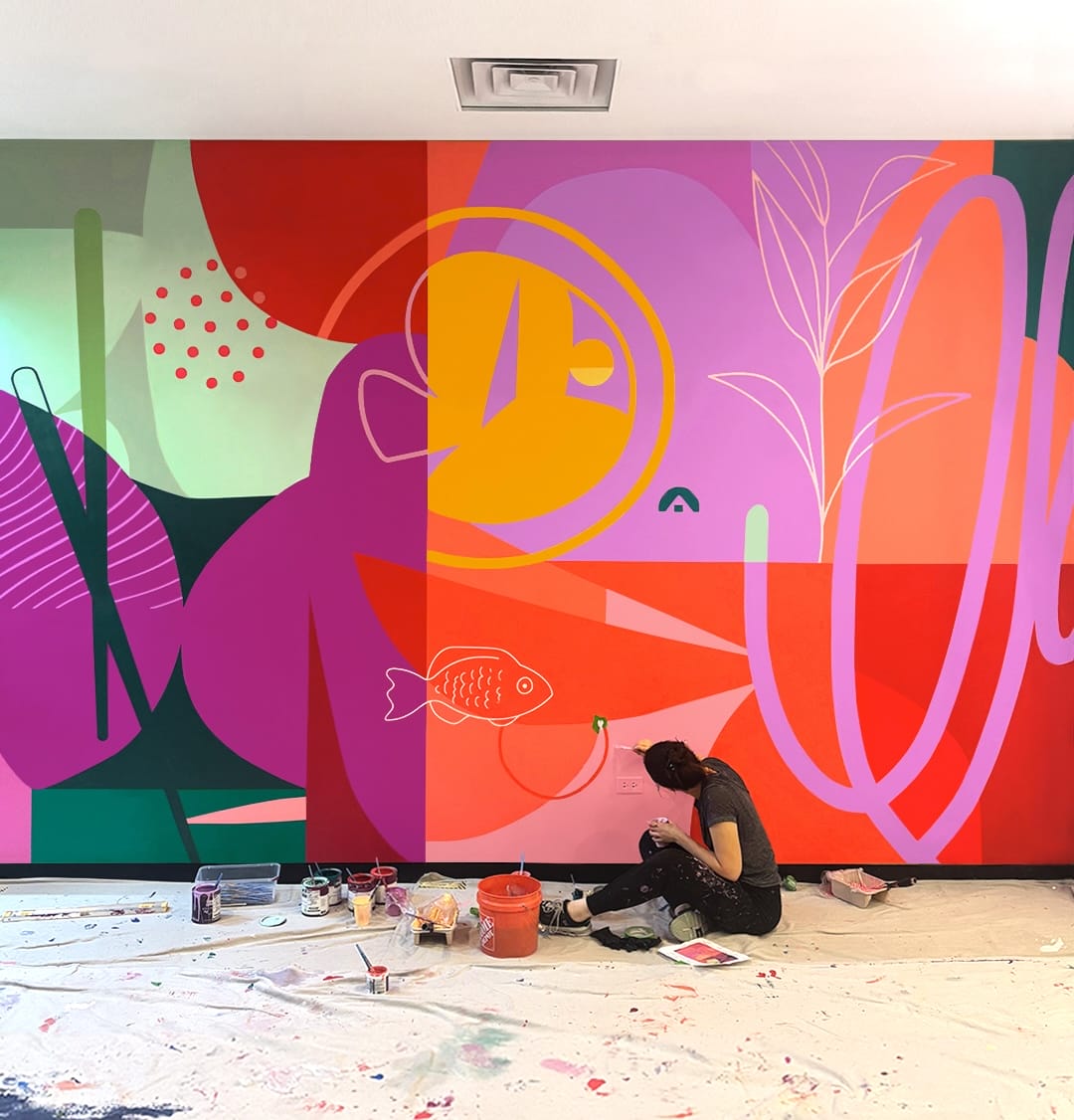 artist Emmy Star Brown is seated at the base of a colorful abstract mural as she puts on finishing touches