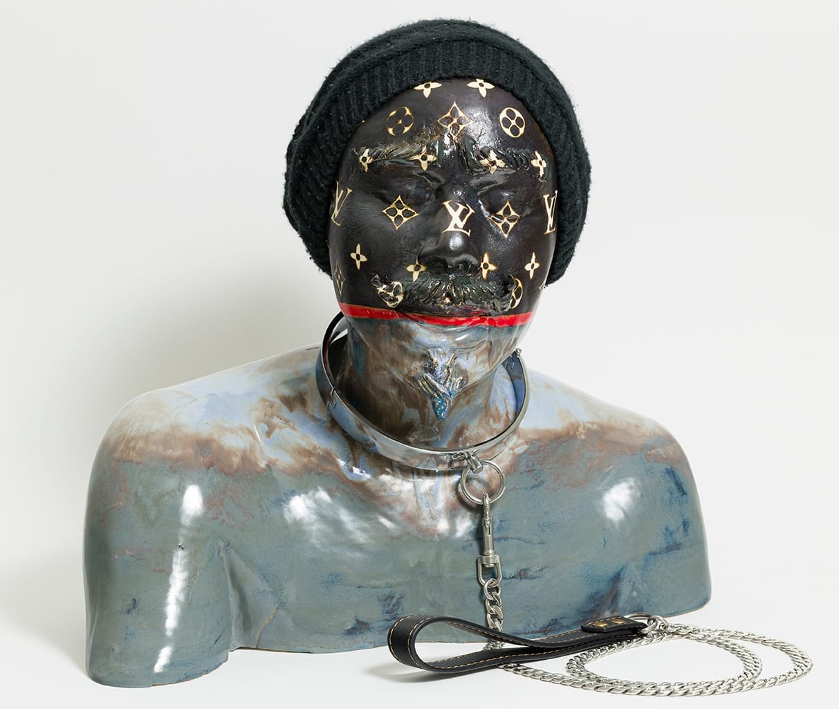 a ceramic bust of a Black man with shackles around his neck, his face covered in the Louis Vuitton logo, wearing a black beanie