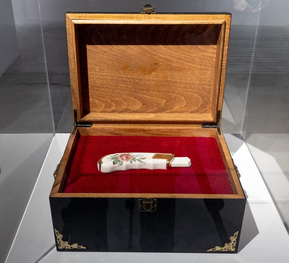 a wooden box with a velvet interior holds a box cutter made of ceramic with a floral design