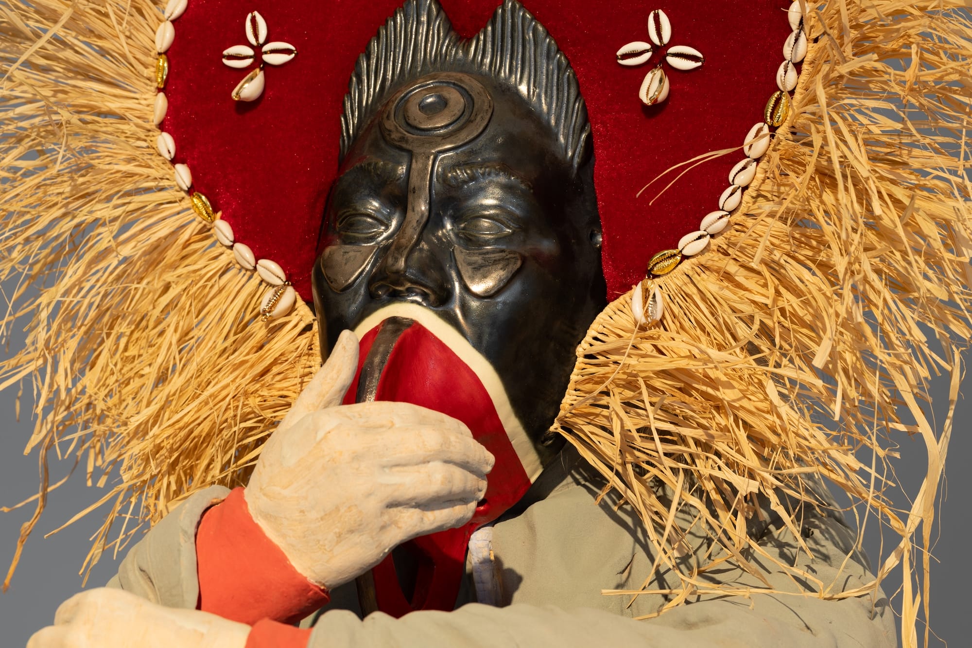 a detail of a large sculpture of a Black figure with an ornate headdress, their hand holding a mask-like piece of fabric over their mouth