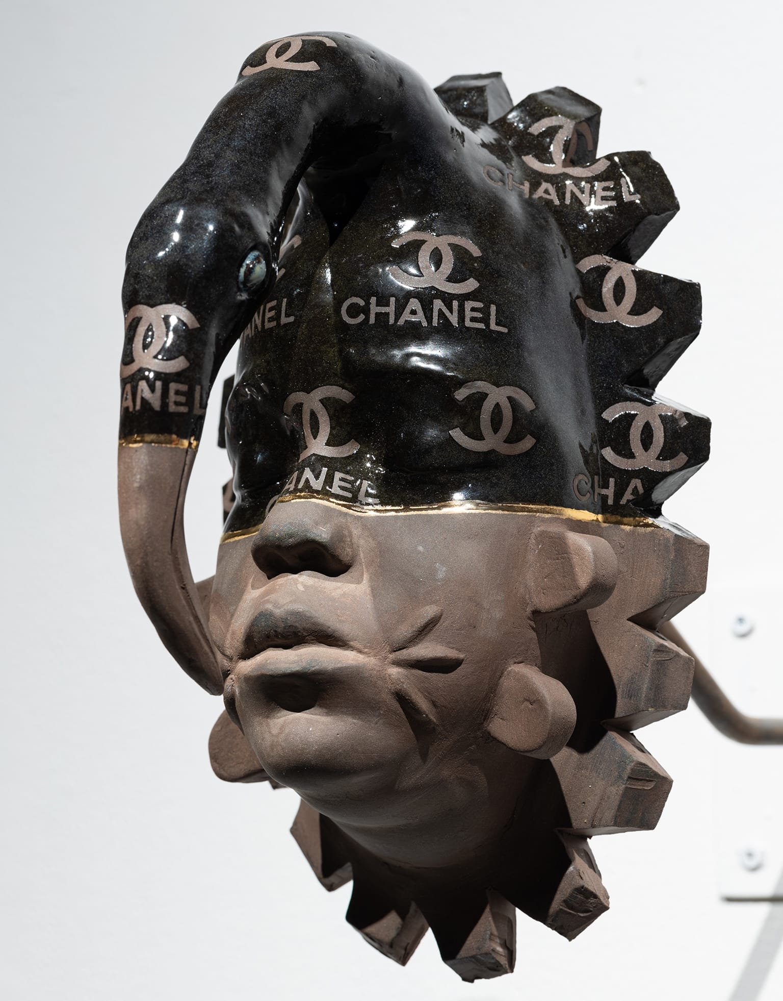 a ceramic wall sculpture of a Black man's head in gray tone, with a black-painted area from the eyes upward including the Chanel logo
