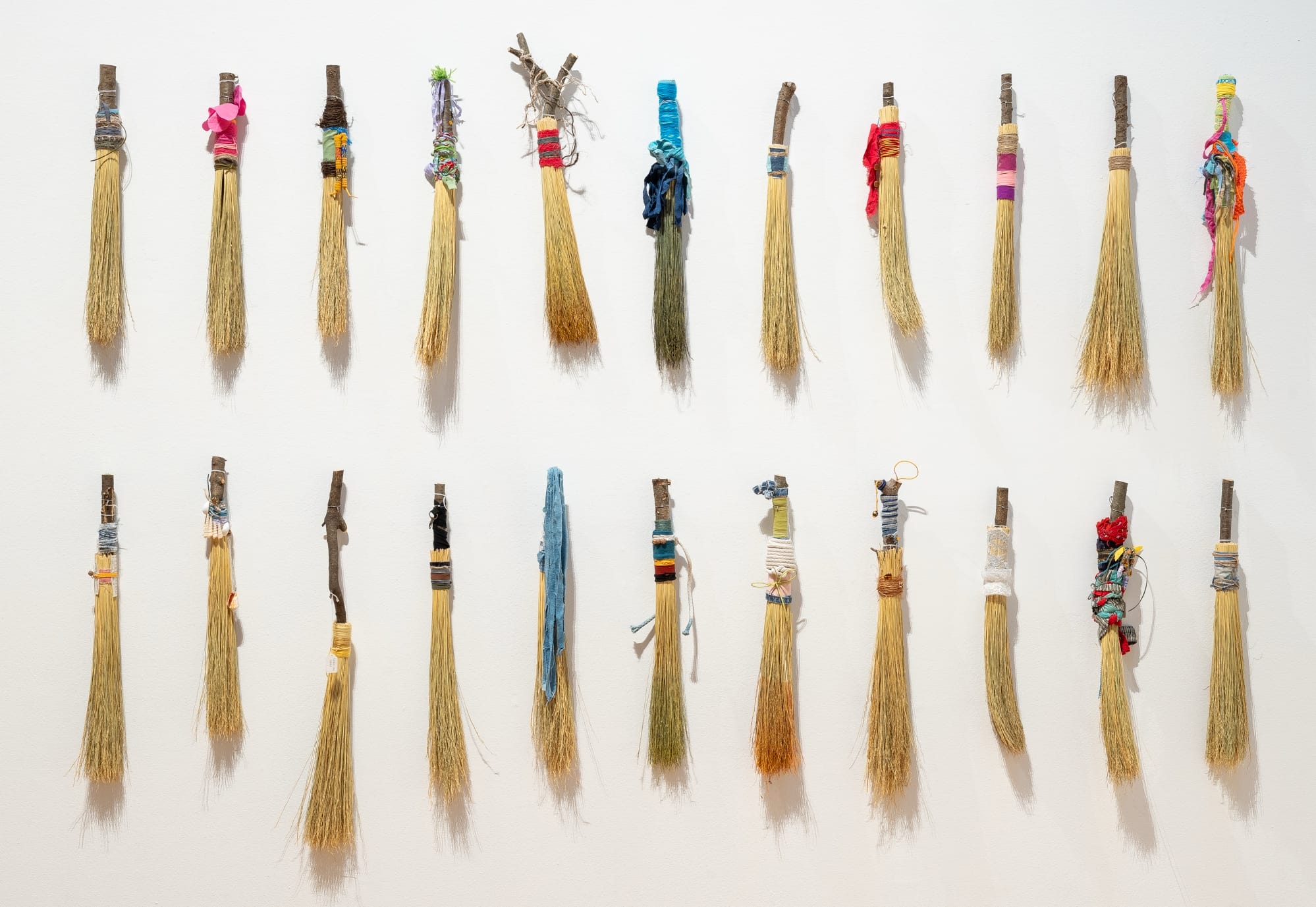 a collection of hand brooms installed in a vertical grid on a white wall