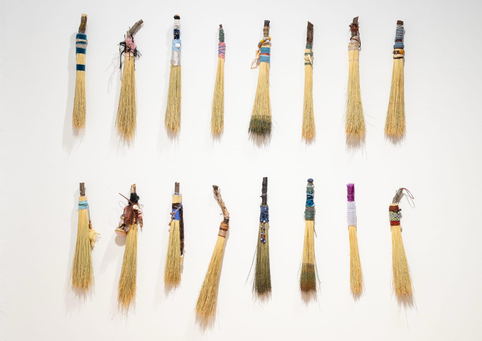 a collection of hand brooms installed in a vertical grid on a white wall