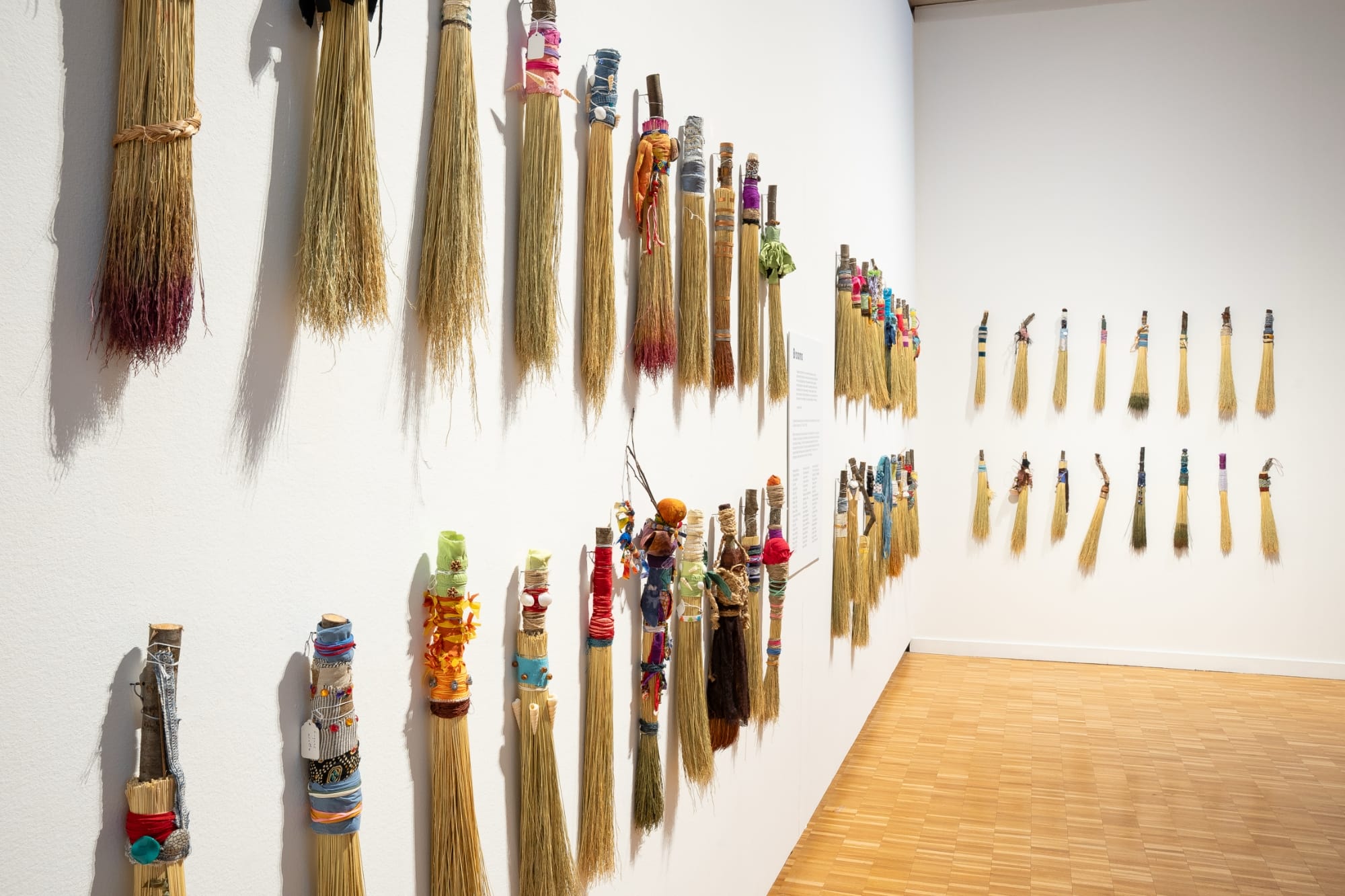 a collection of hand brooms installed in a vertical grid on a white wall