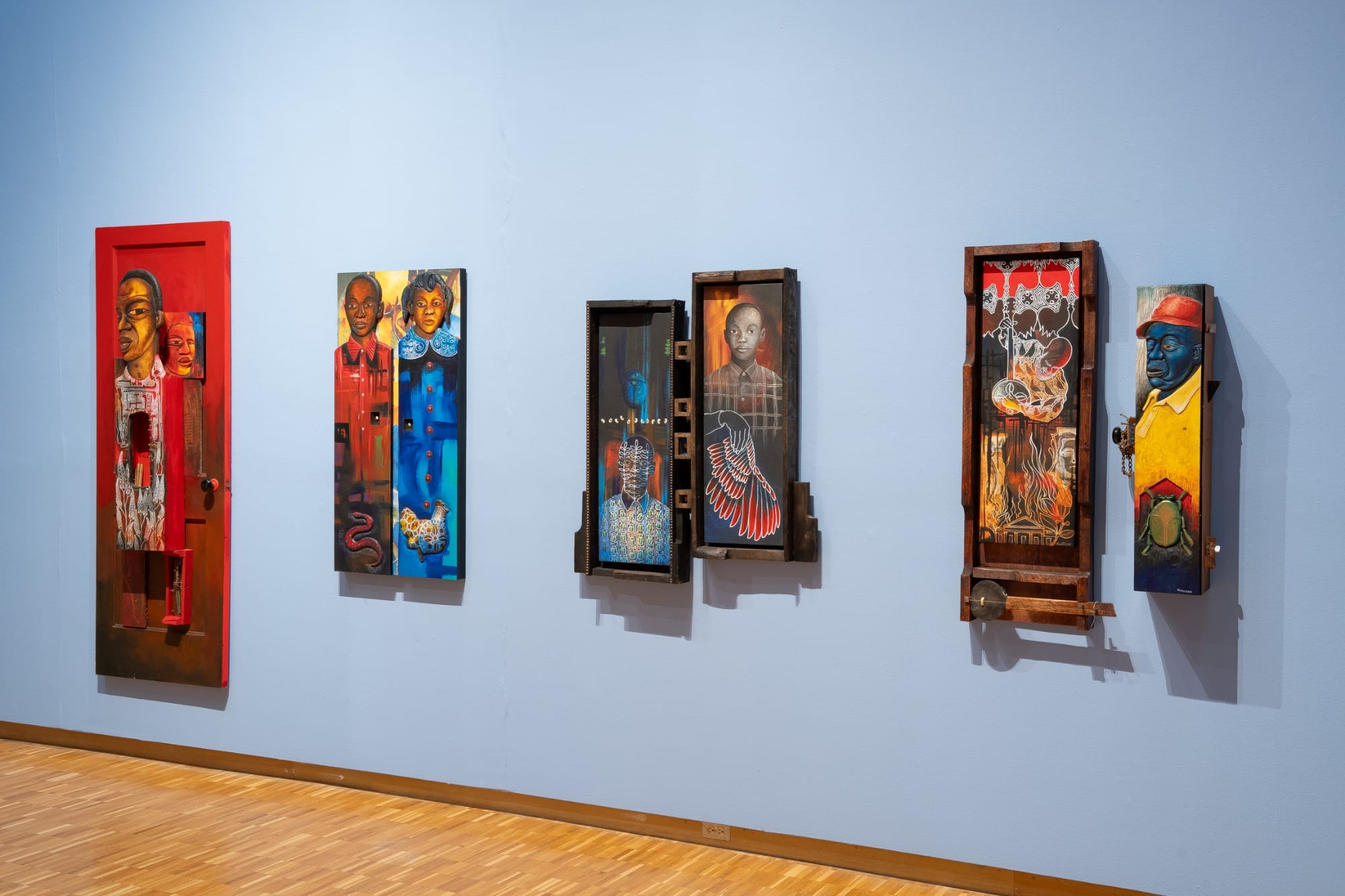 a collection of painted wood wall works by Daniel Minter on a light blue wall