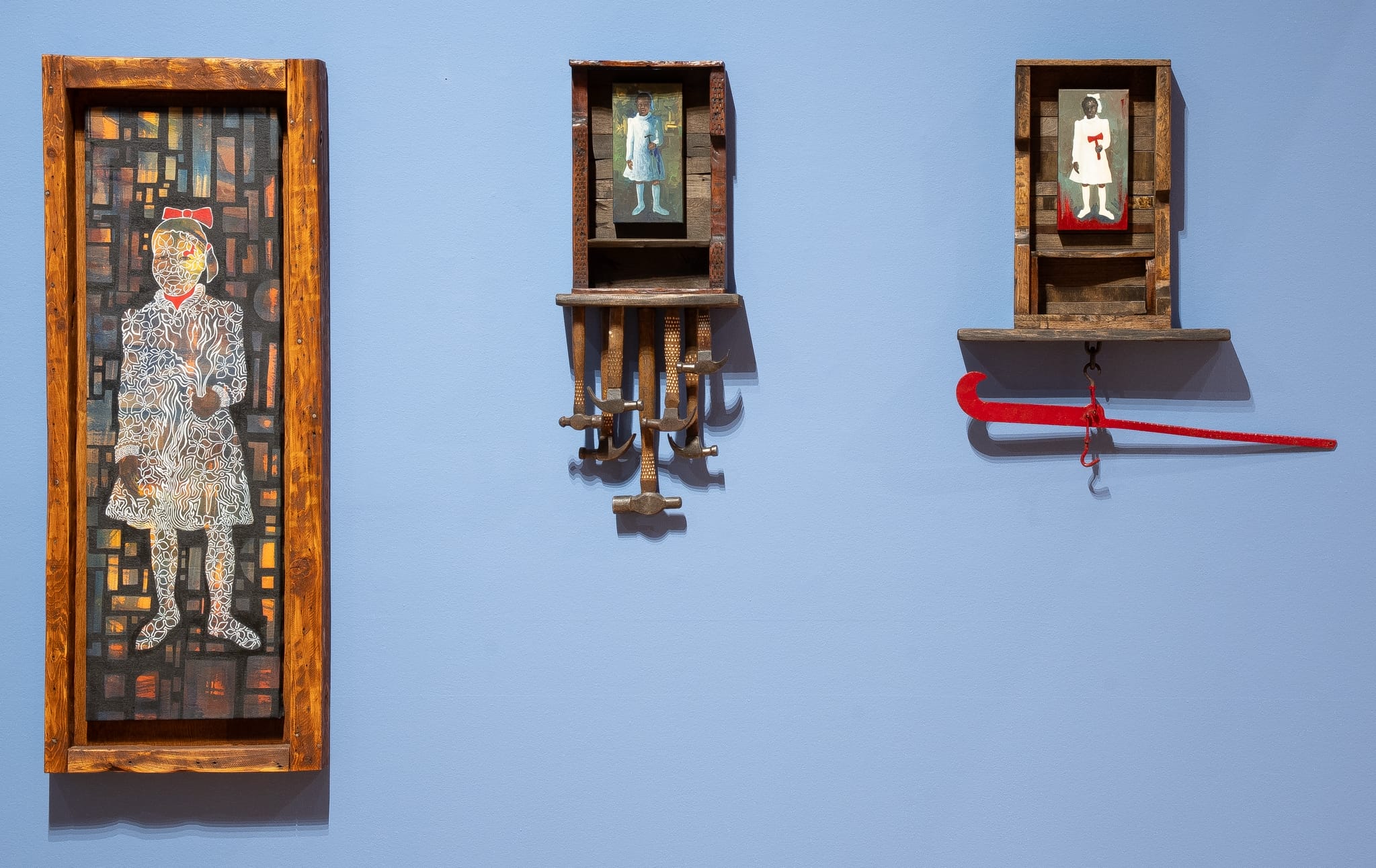 a collection of painted wood wall works by Daniel Minter on a light blue wall