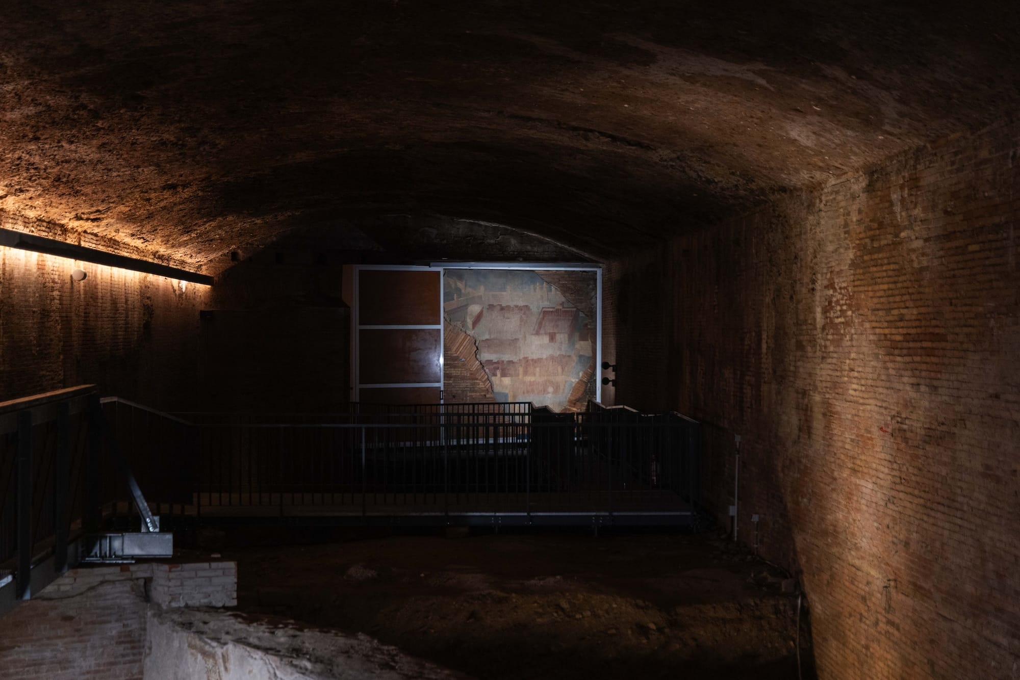 an interior of an ancient Roman domus with an architectural fresco preserved and illuminated in on a distant wall