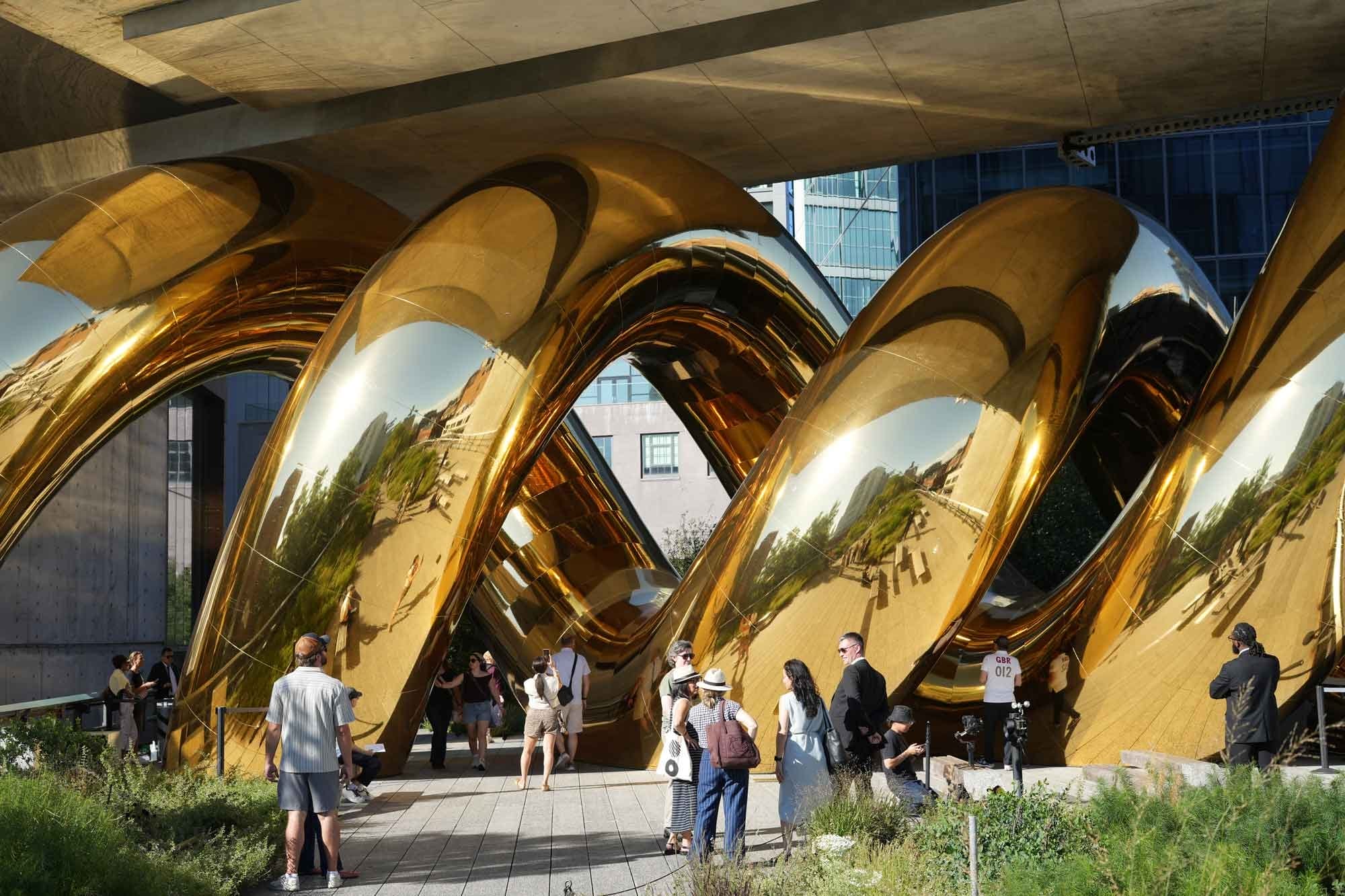 a giant inflatable sculpture of a gold spiral wedged beneath an overpass on the High Line in Manhattan