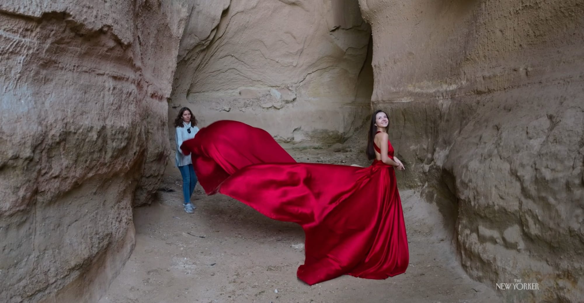 a still of a woman fluffing another's dress in a cavern