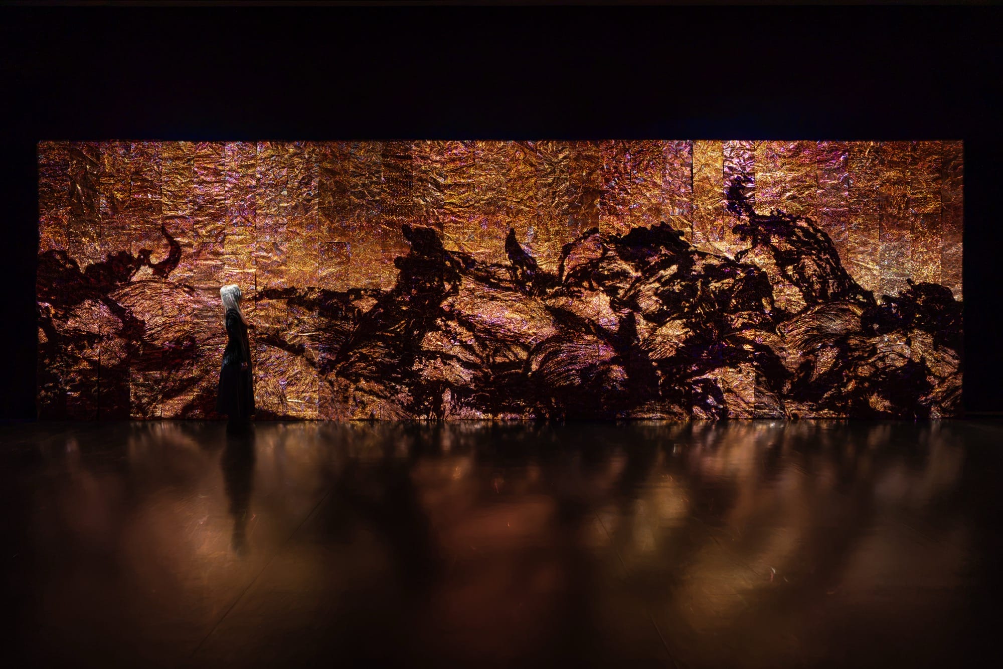 a person stands in front of an installation of hammered copper with a digital projection on top