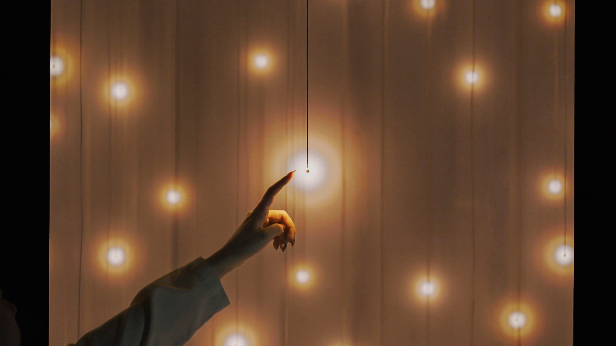 a hand reaches out to touch a small glowing bulb