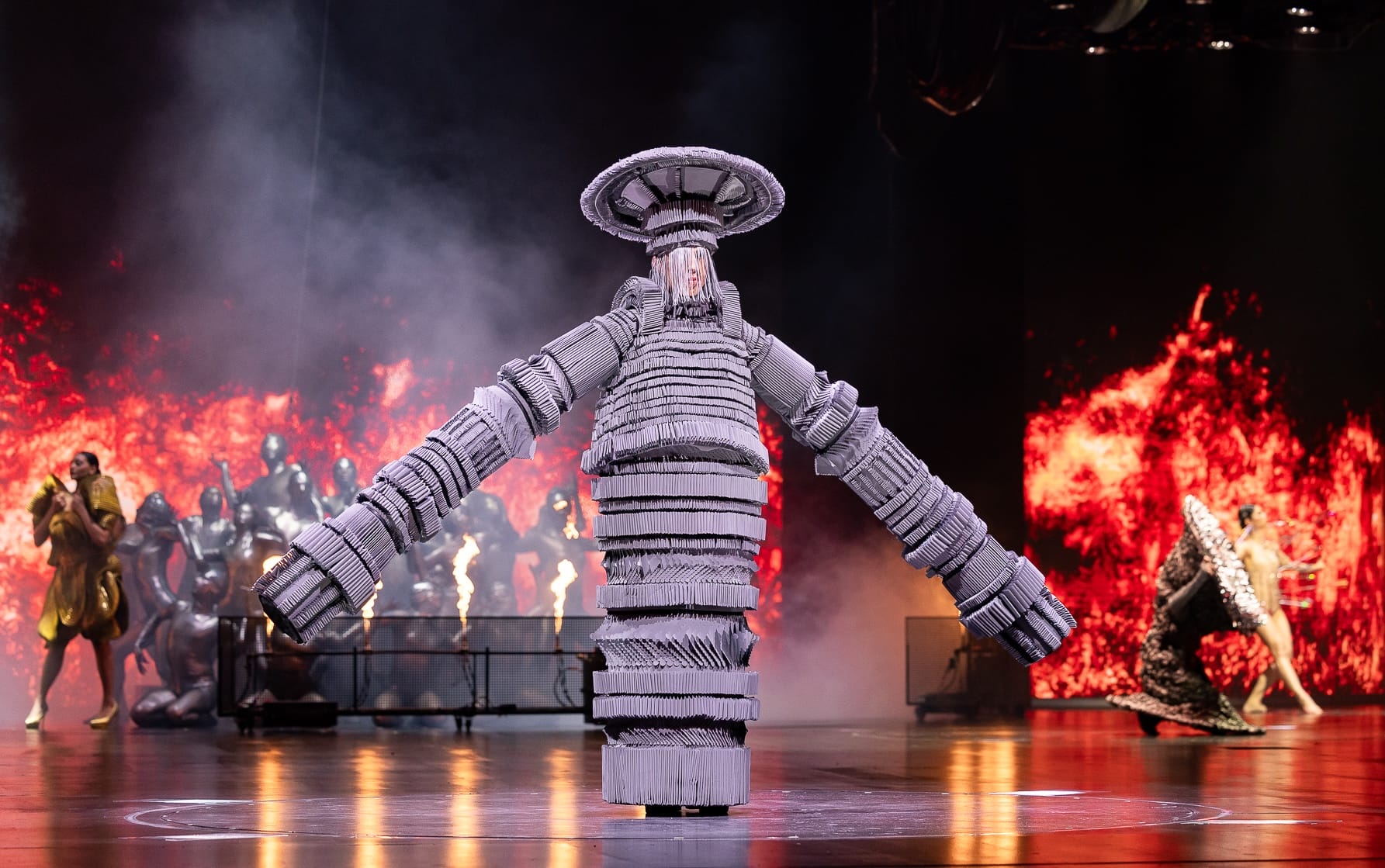 an elaborate garment being performed on stage in the form of a very long-armed, cylindrical, abstract figure with a disk-like head