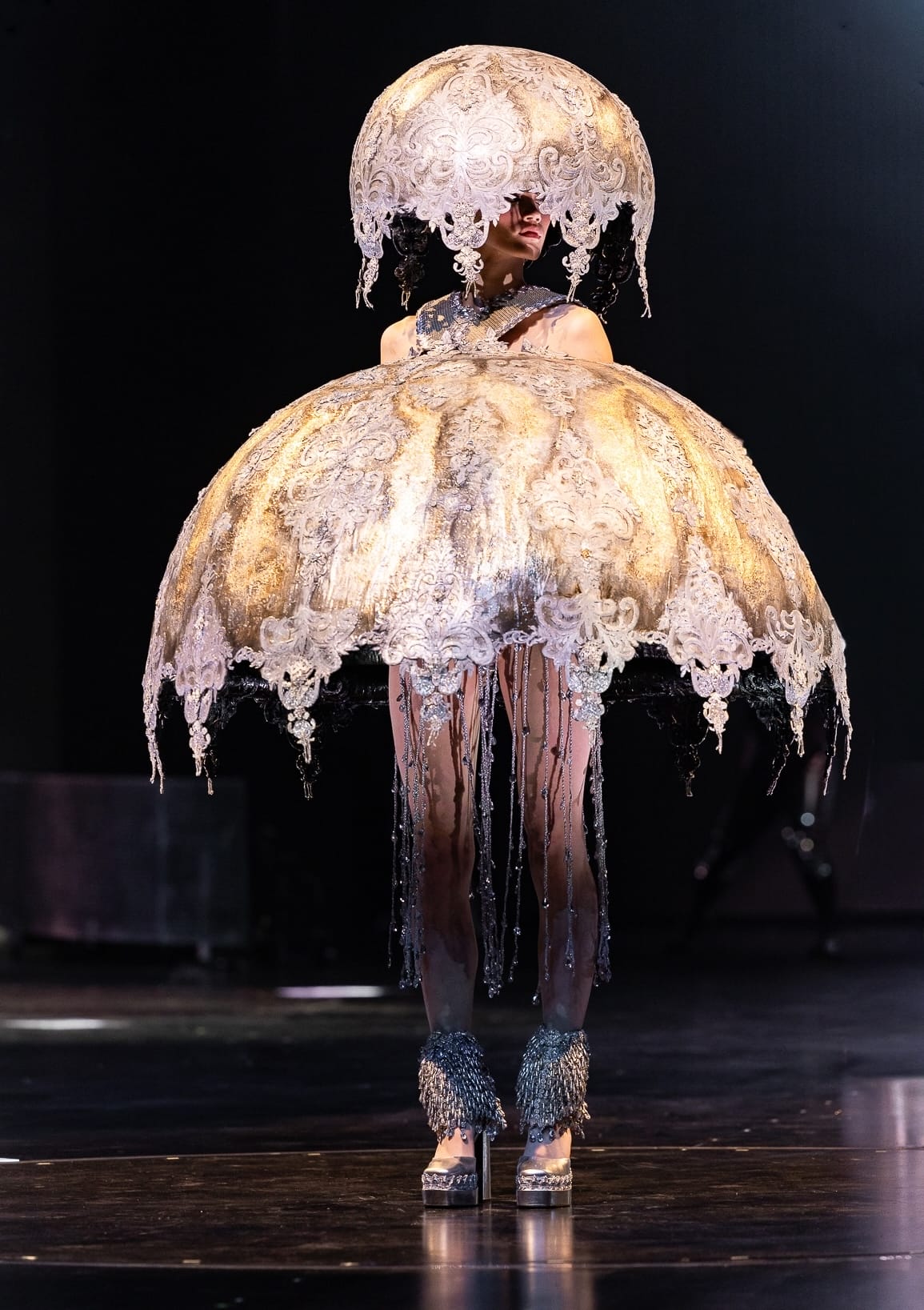 an elegant, avant-garde, handmade garment with draping, lacy, mushroom cap-like forms on the head and around the body