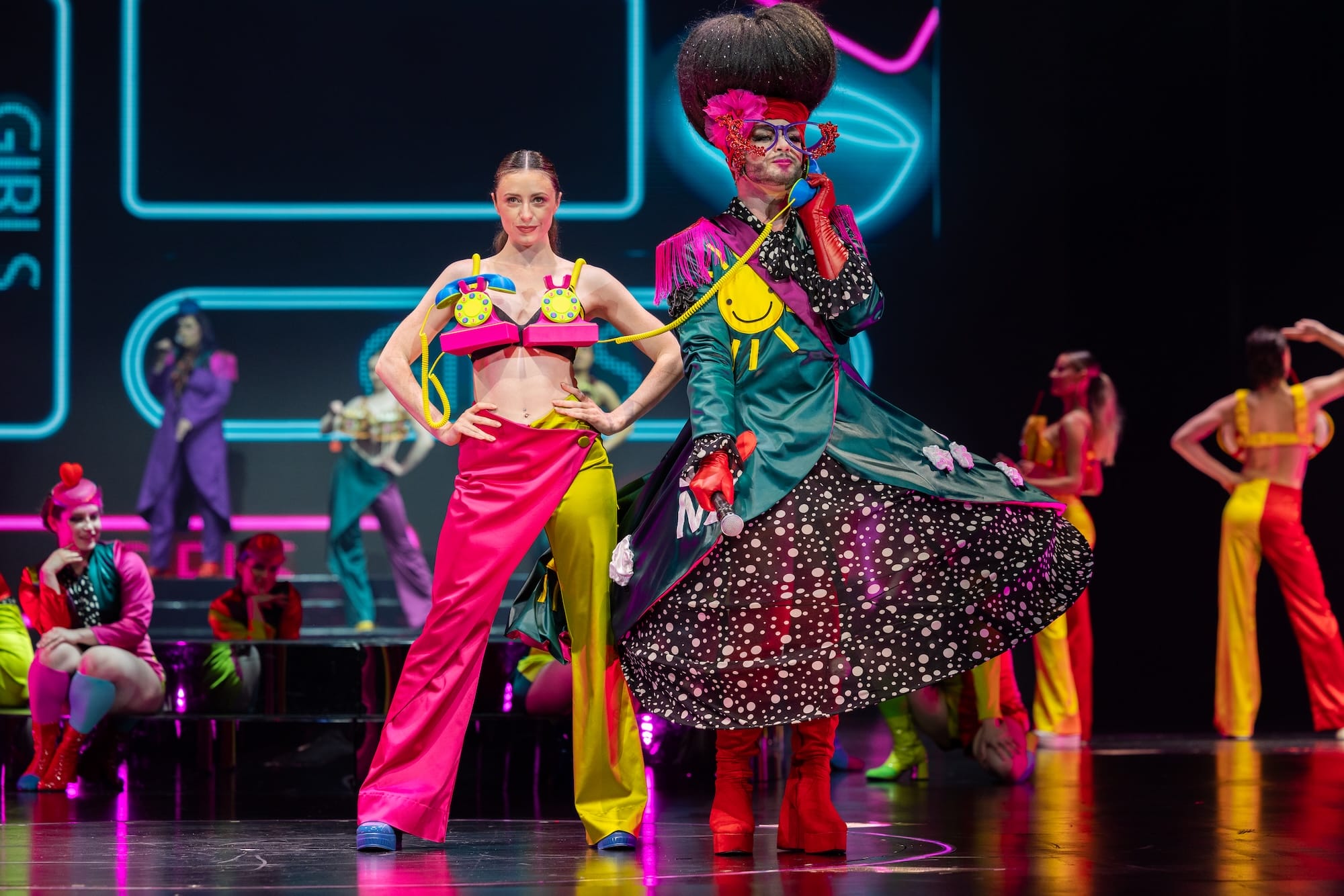two people in a duo costume-garment, one with telephones on her top and the other in an elaborate petticoat-type outfit, talking on one of the phones