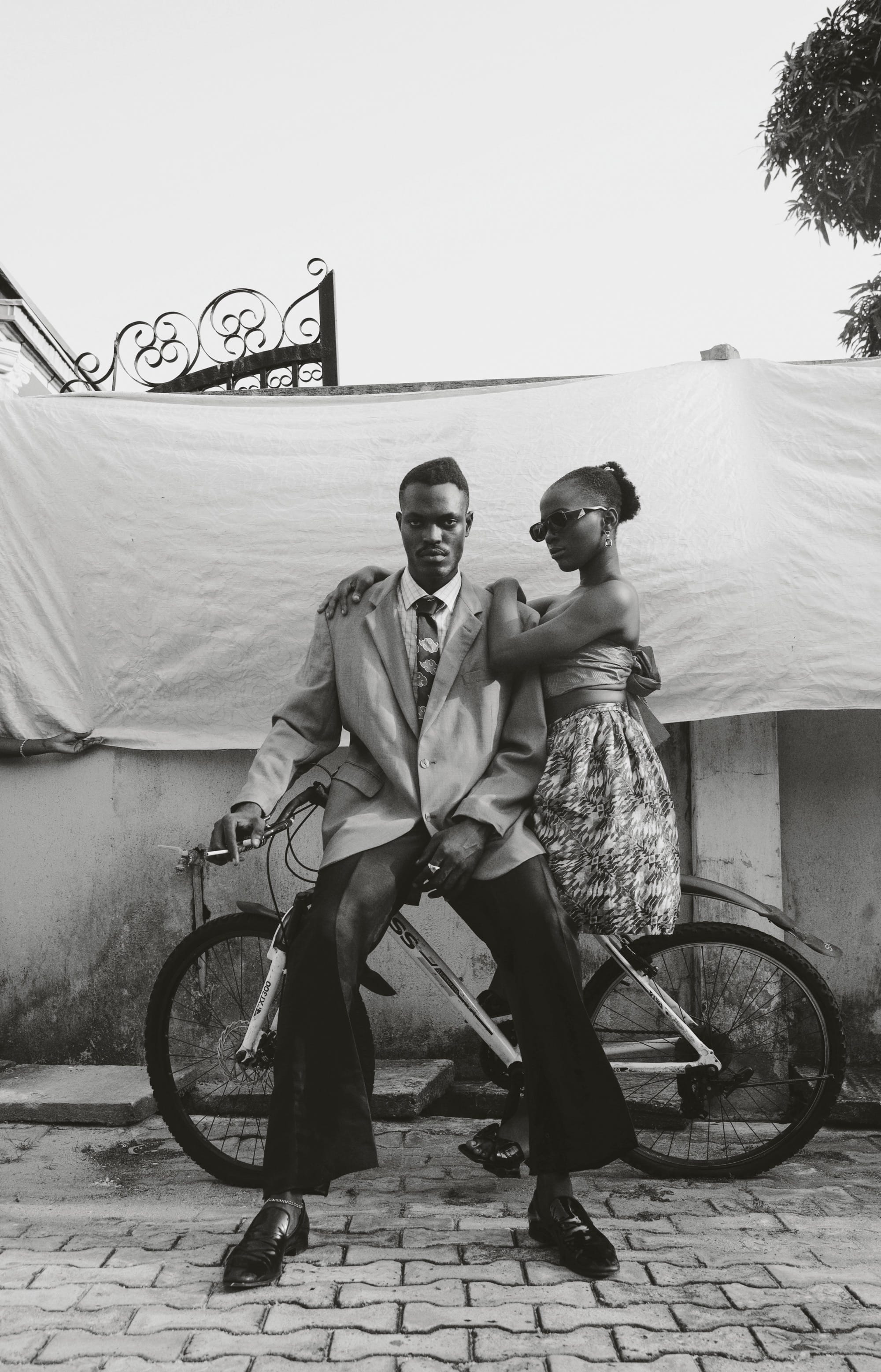 a black and white photo of a couple dressed up and perched sideways on a bicycle