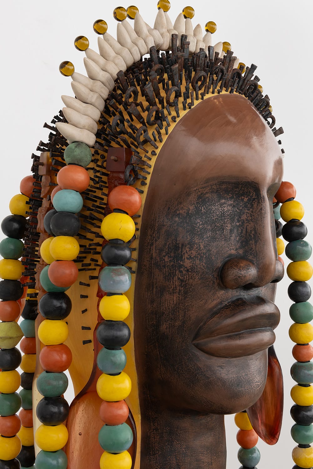 a large sculpture of a stylized Black figure's head, inspired by African masking traditions, with large colorful beads draped like hair or a headdress