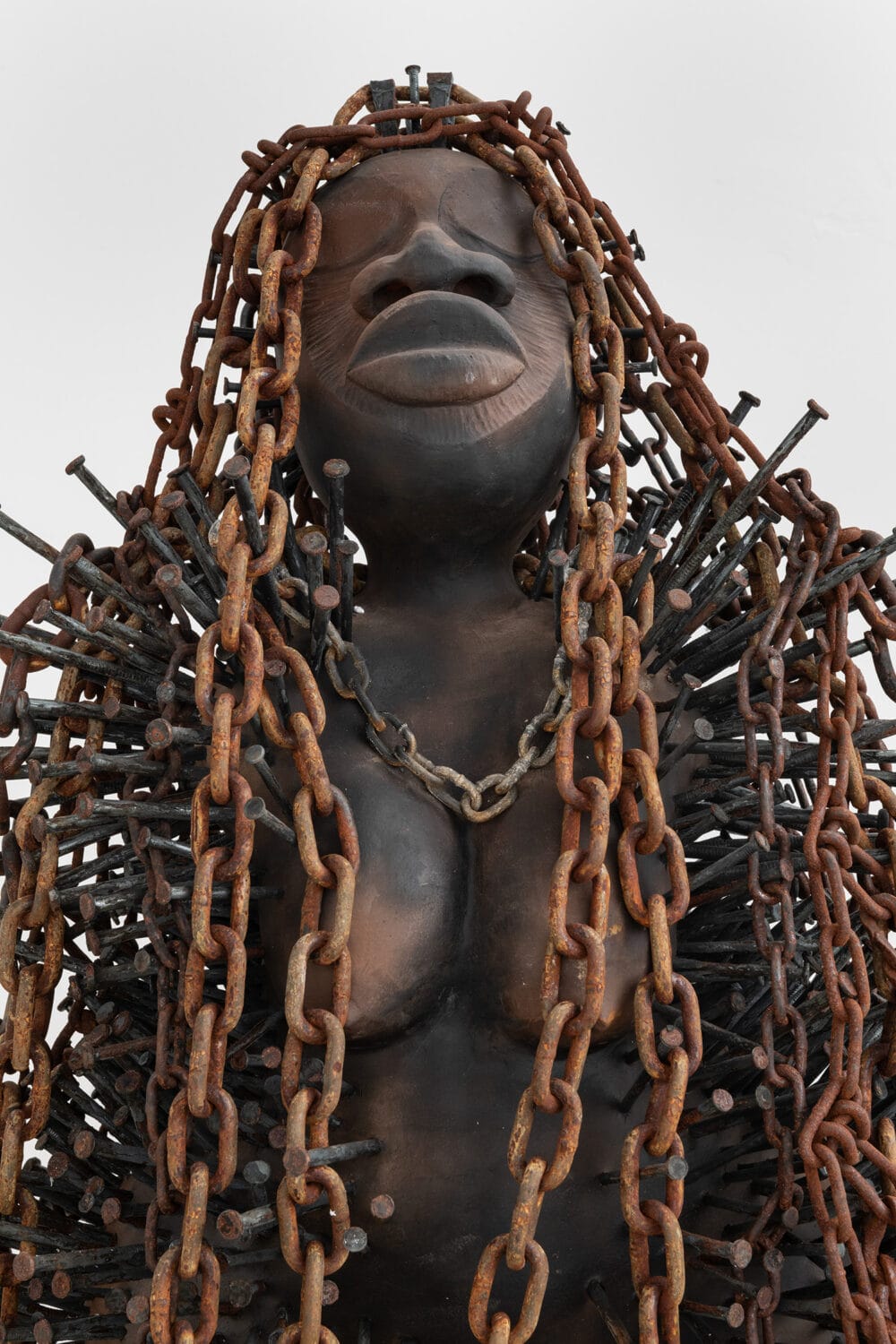 a sculpture of a stylized Black figure with rusty chains for hair and nails in the shoulders that appear cloak-like