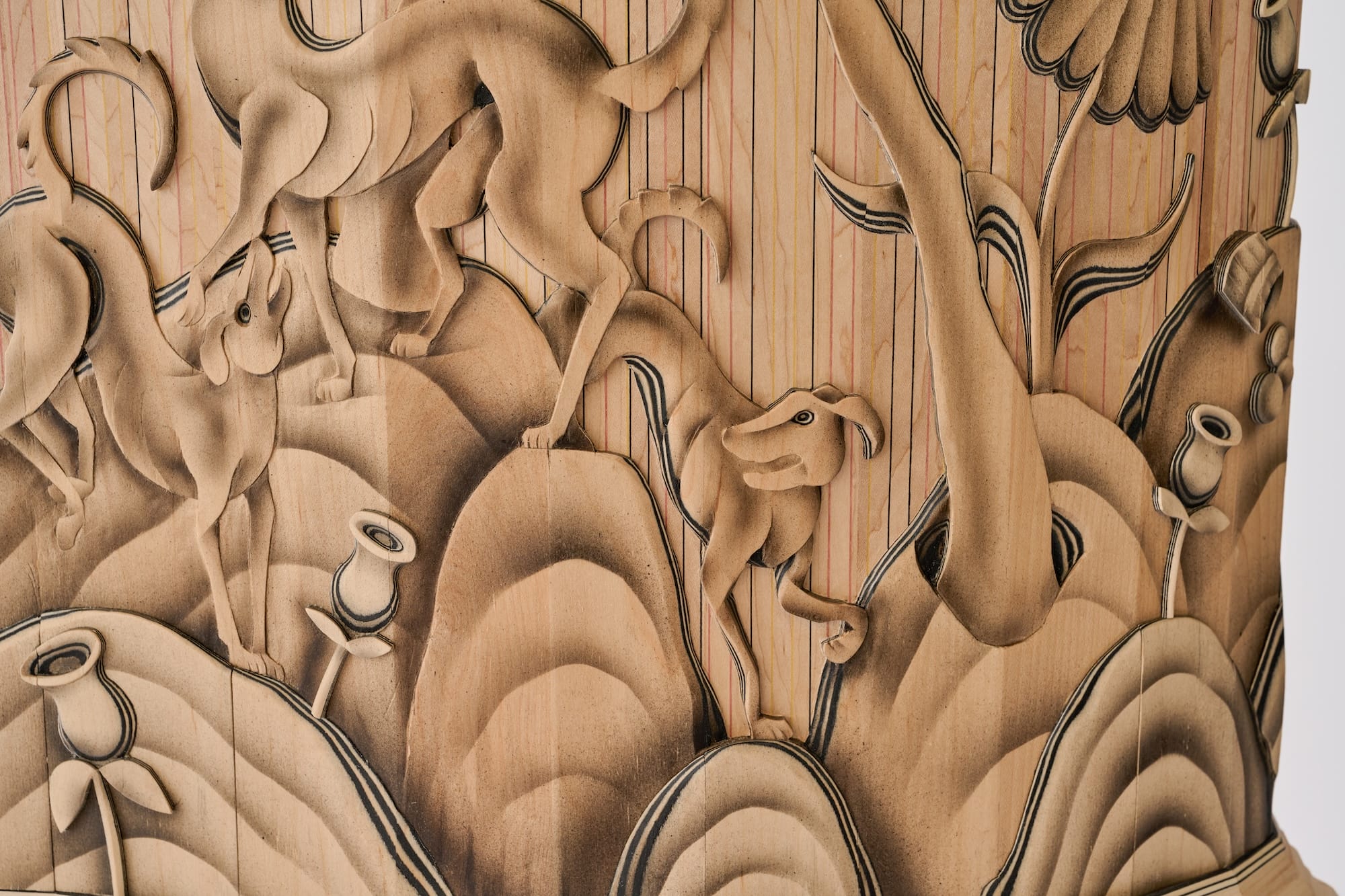 a detail of a large wooden cabinet that resembles a giant vessel, with crewel-inspired wood carving on the exterior featuring plants and animals