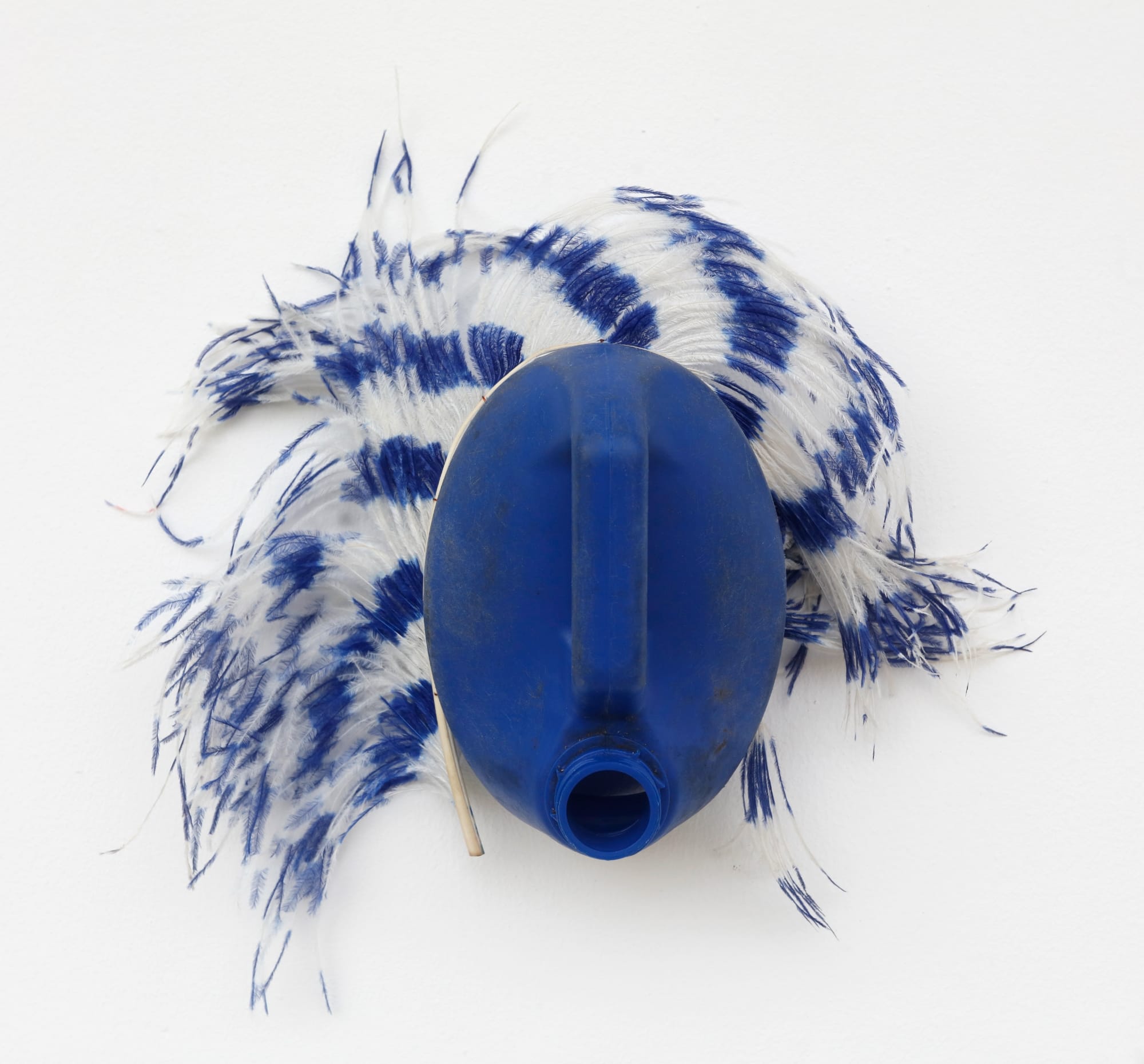 an abstract mask-like sculpture made of a blue plastic jug and blue and white feathers