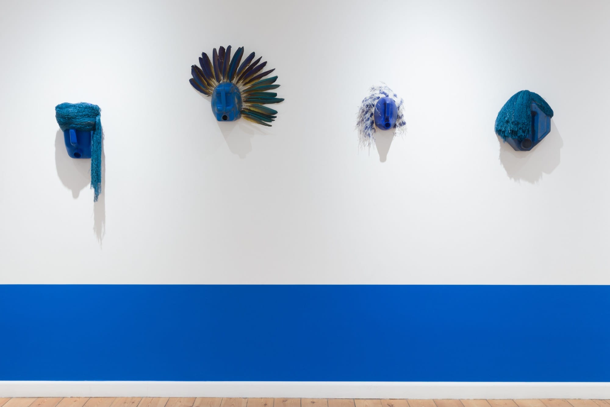 an installation view of four blue mask sculptures on a wall above a bold cobalt stripe