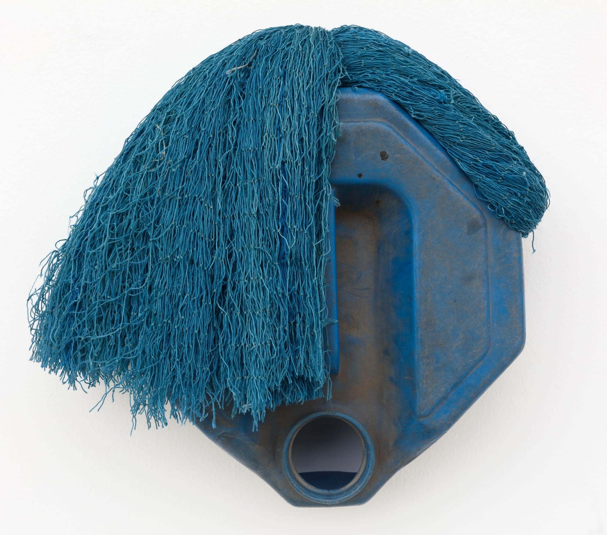 an abstract mask-like sculpture made of a blue plastic jug and blue netting