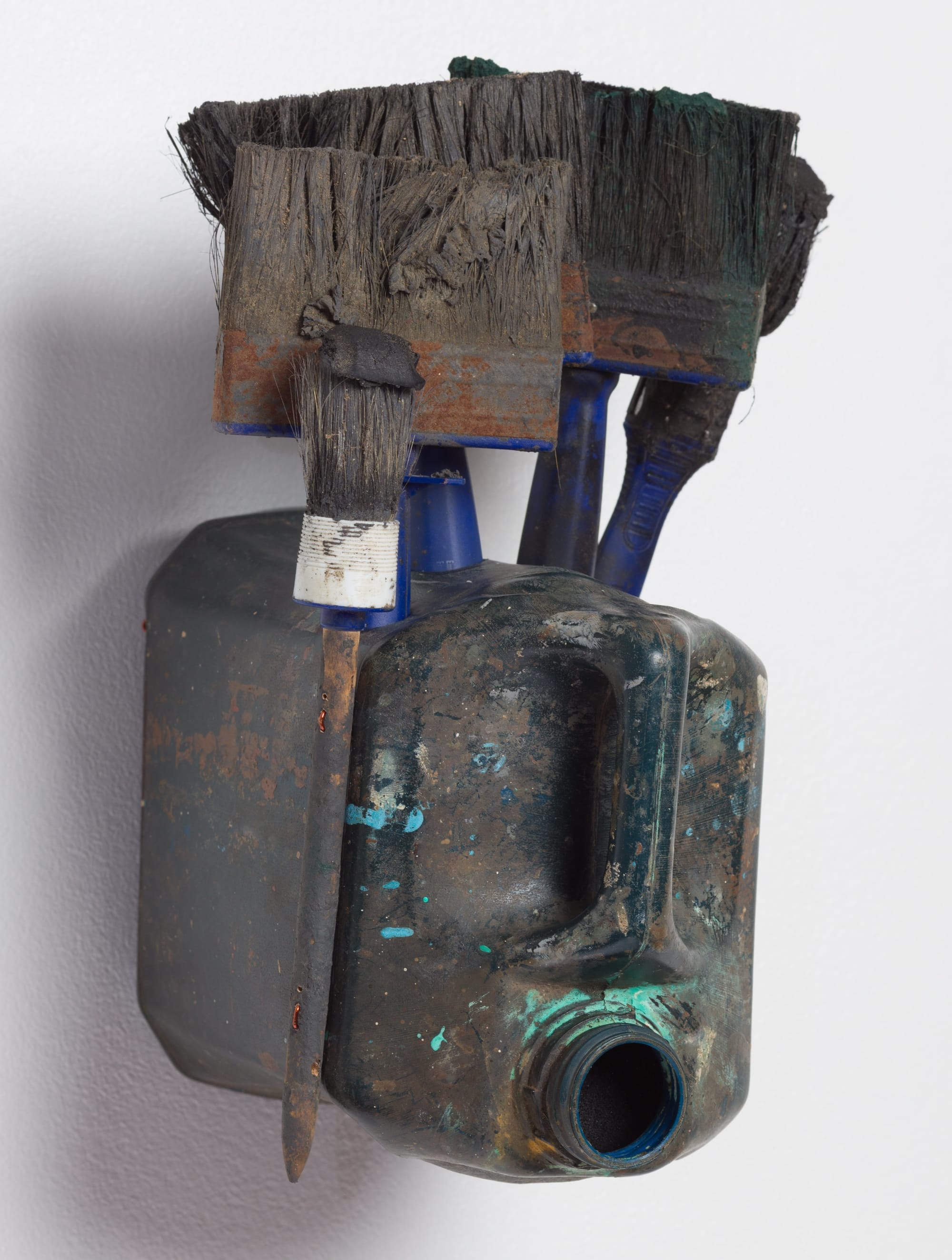 an abstract mask-like sculpture made of a gray plastic jug and used paintbrushes