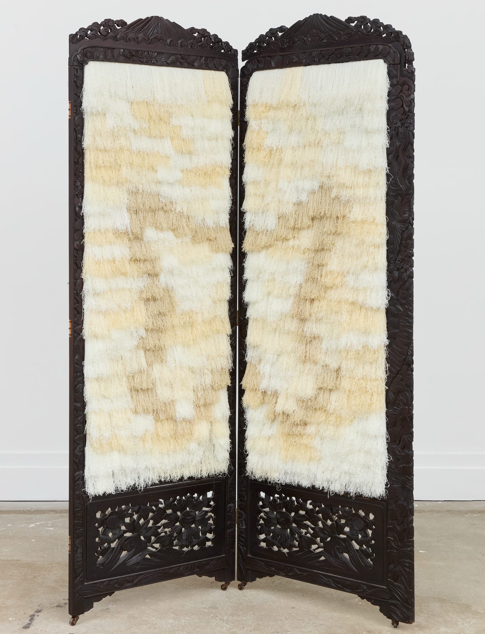 an ornately carved wooden folding screen with white and beige fur as the panels