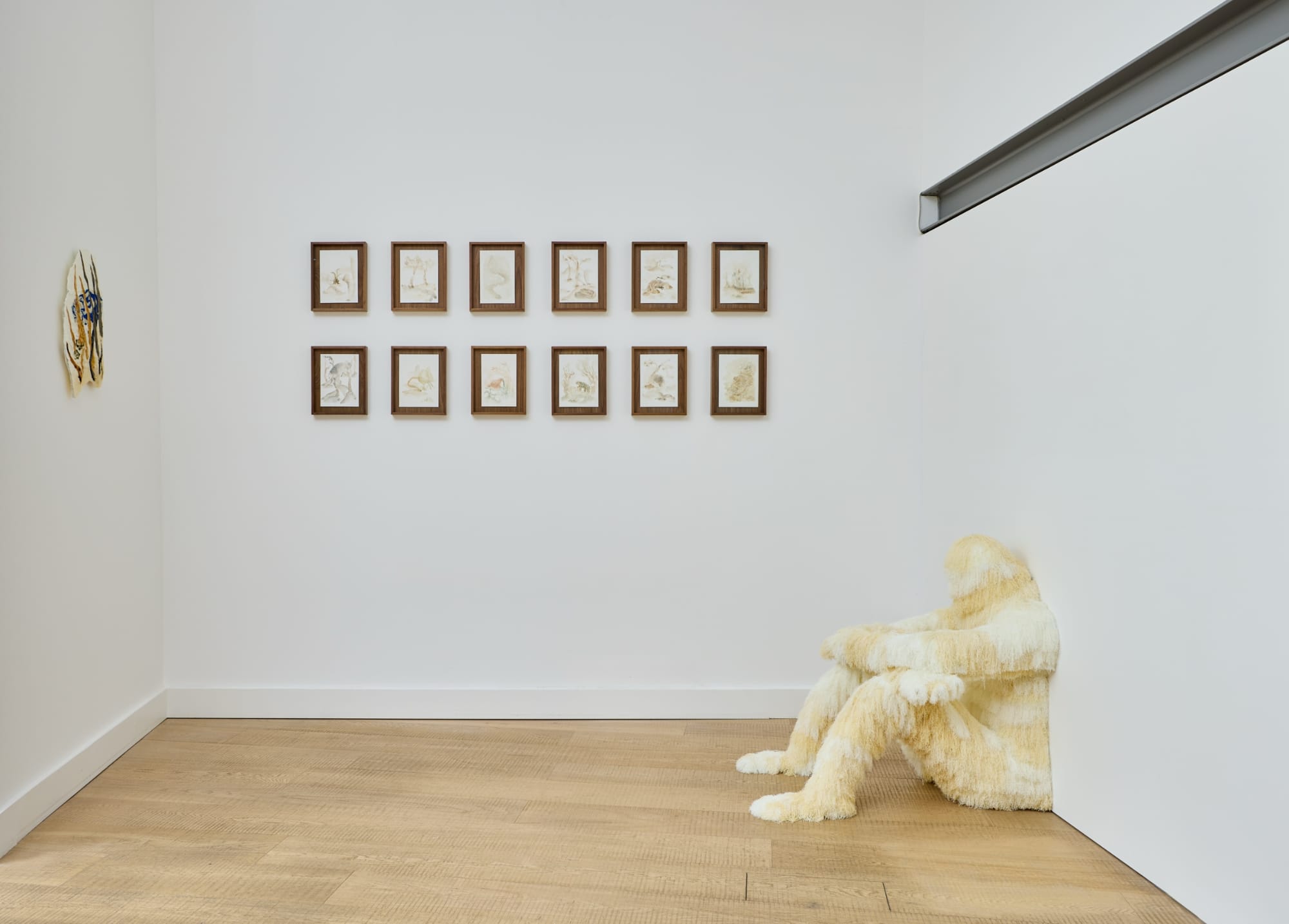an installation shot with several small wall works and a large, fur covered seated figure