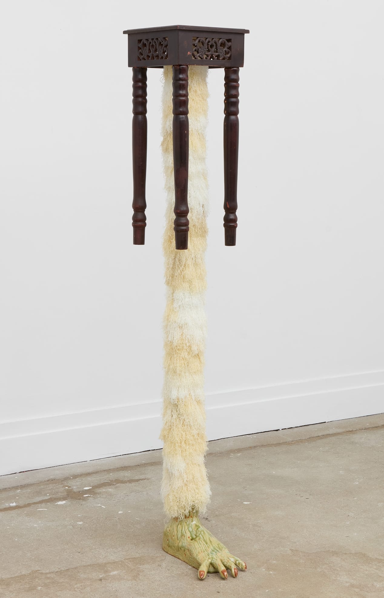 a leg-like fur covered sculpture with a ceramic foot with a small wooden table at the top of the leg