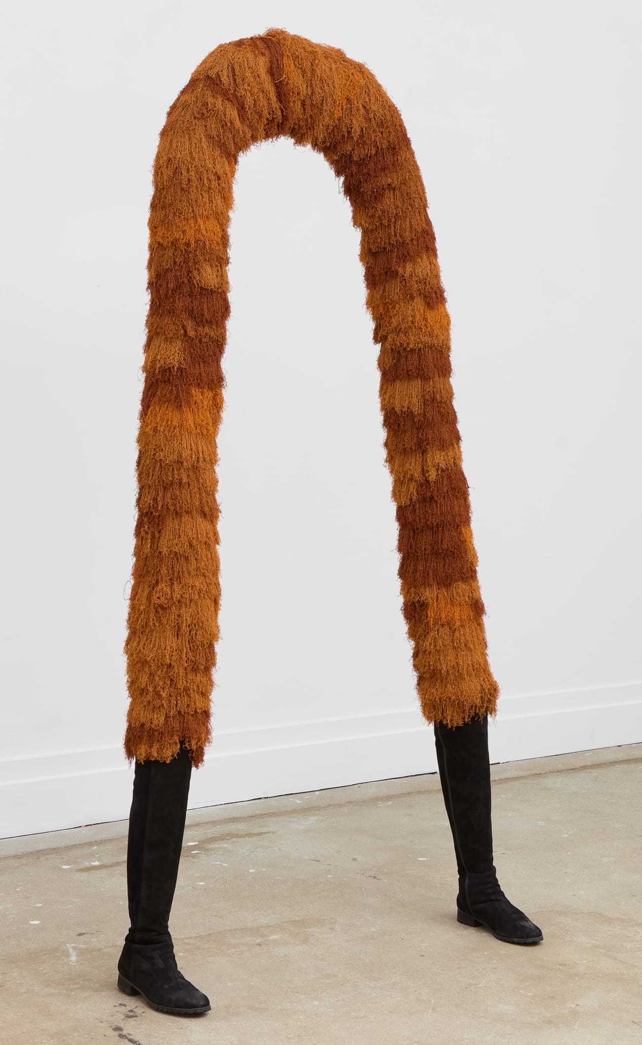 a creature-like sculpture made of a an ochre, textile-covered arch with two feet emerging from the bottom