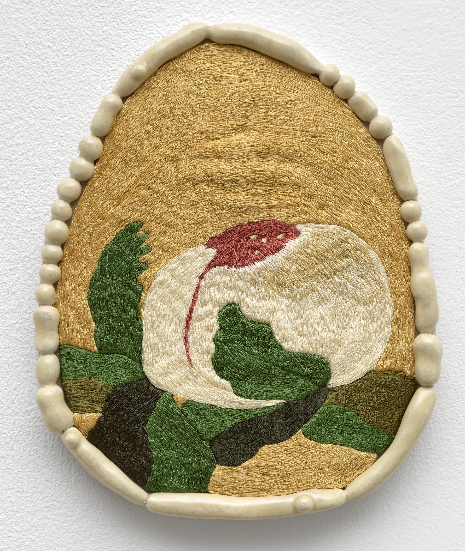 a wall piece by Woo Jin Joo of an embroidered flower with a beige circular ceramic frame