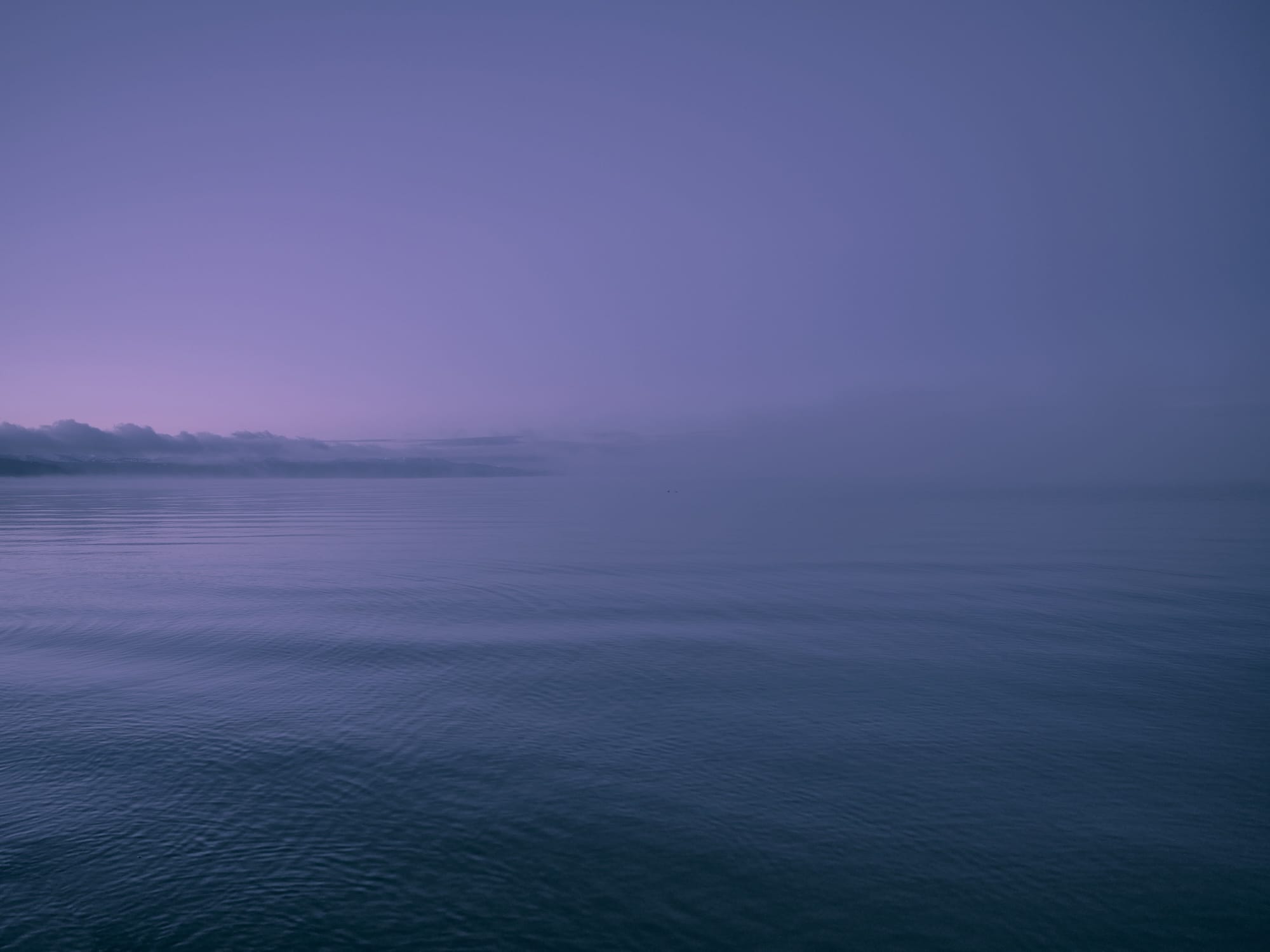 an open body of water with a slice of land in the distance, hued purple at sunrise