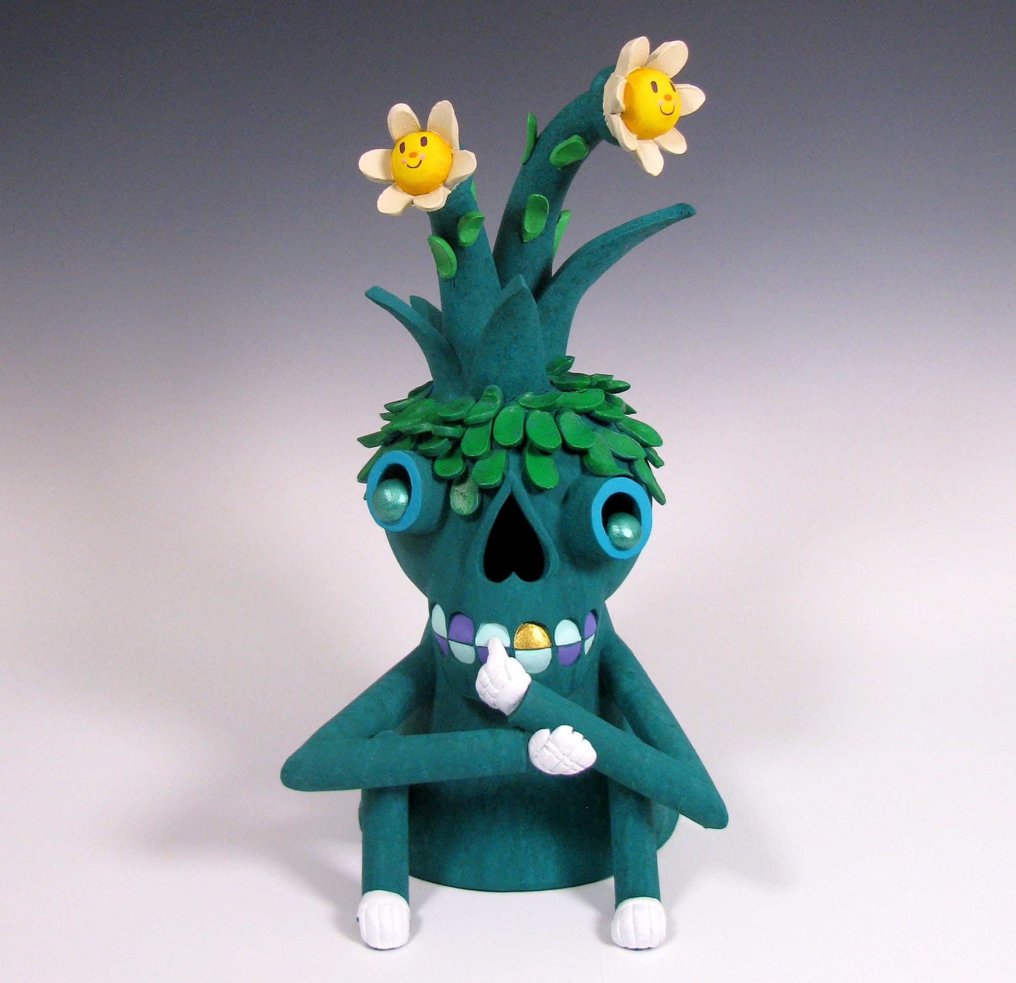 a small green sculpture of a cartoonish figure with two flowers growing out of its head and a skeletal face