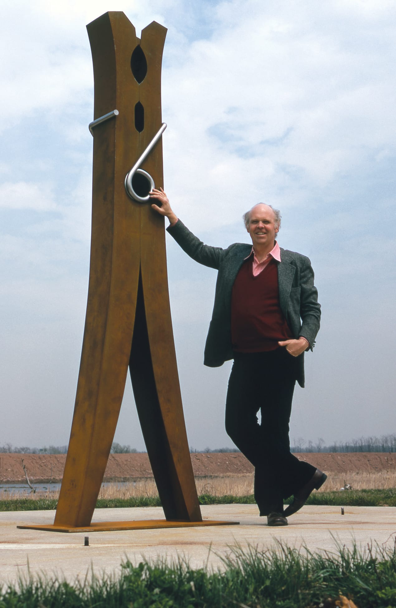 a historical photograph of artist Claes Oldenburg standing beside a giant, 10-foot clothespin sculpture