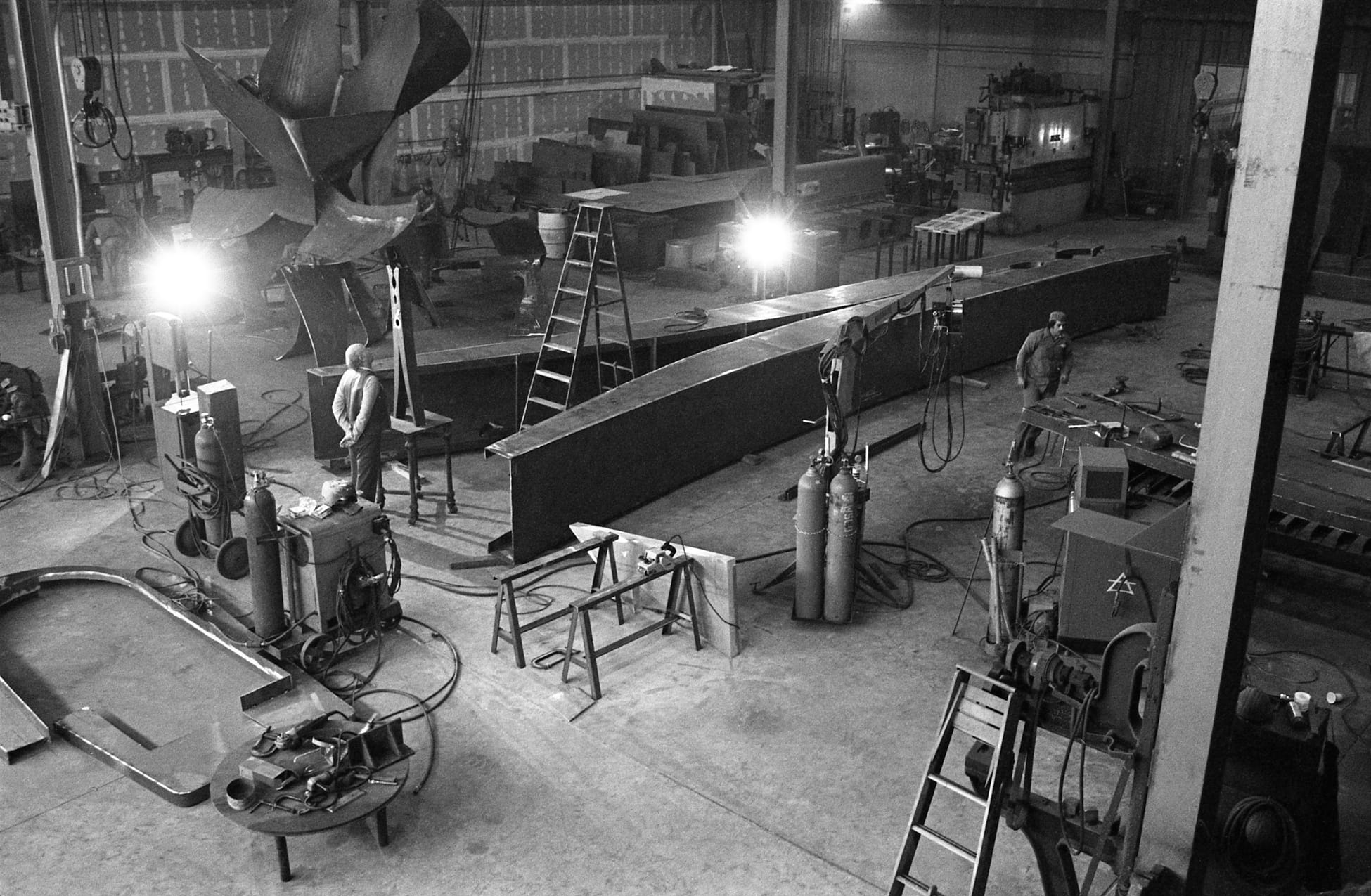 a historical black-and-white photograph of a giant clothespin sculpture by Claes Oldenburg being fabricated in a large space