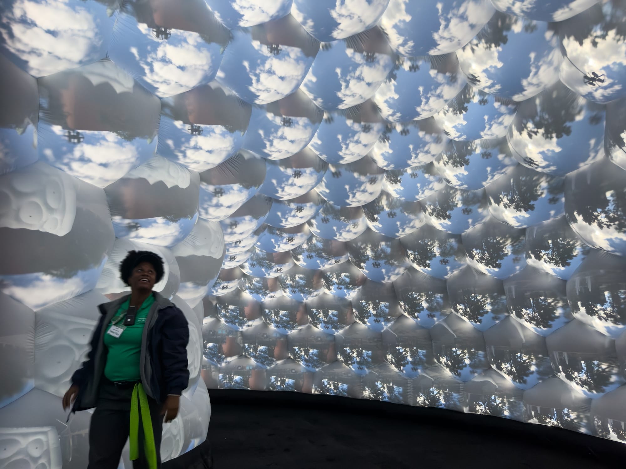 the interior of an architectural, inflatable compound camera installation with a person standing inside it, looking up at bubble-like forms featuring images of outside captured by tiny apertures