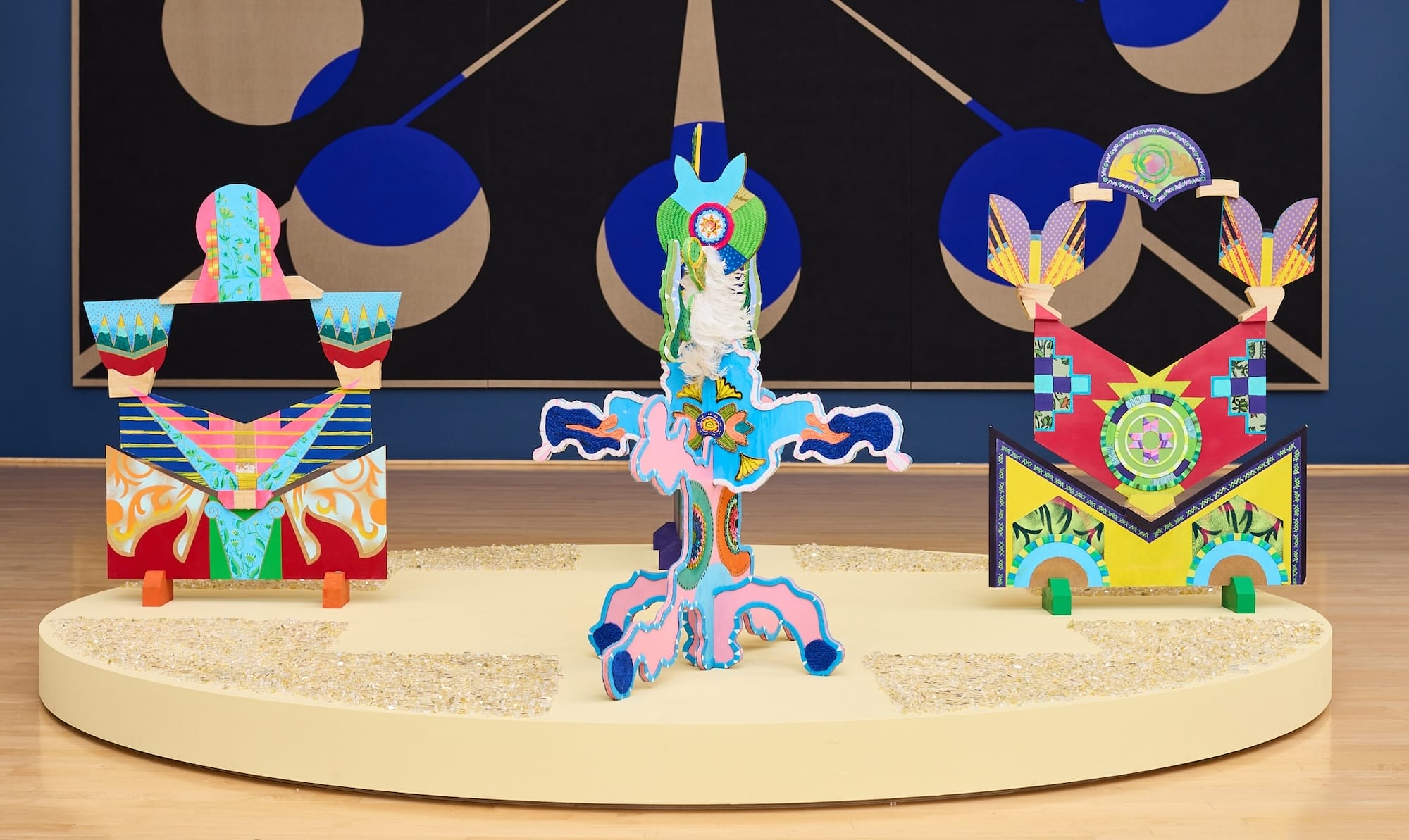 A series of colorful, geometric sculptures in front of a large geometric painting