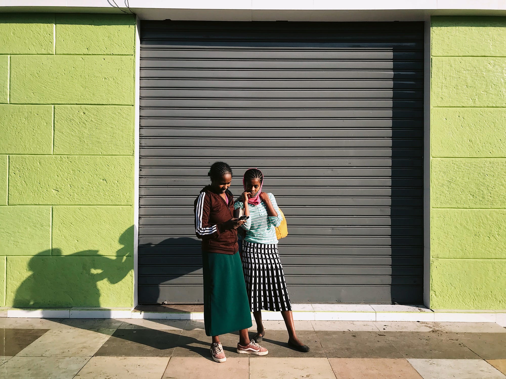 two young people stand in front of a gray garage door surrounded by lime green walls