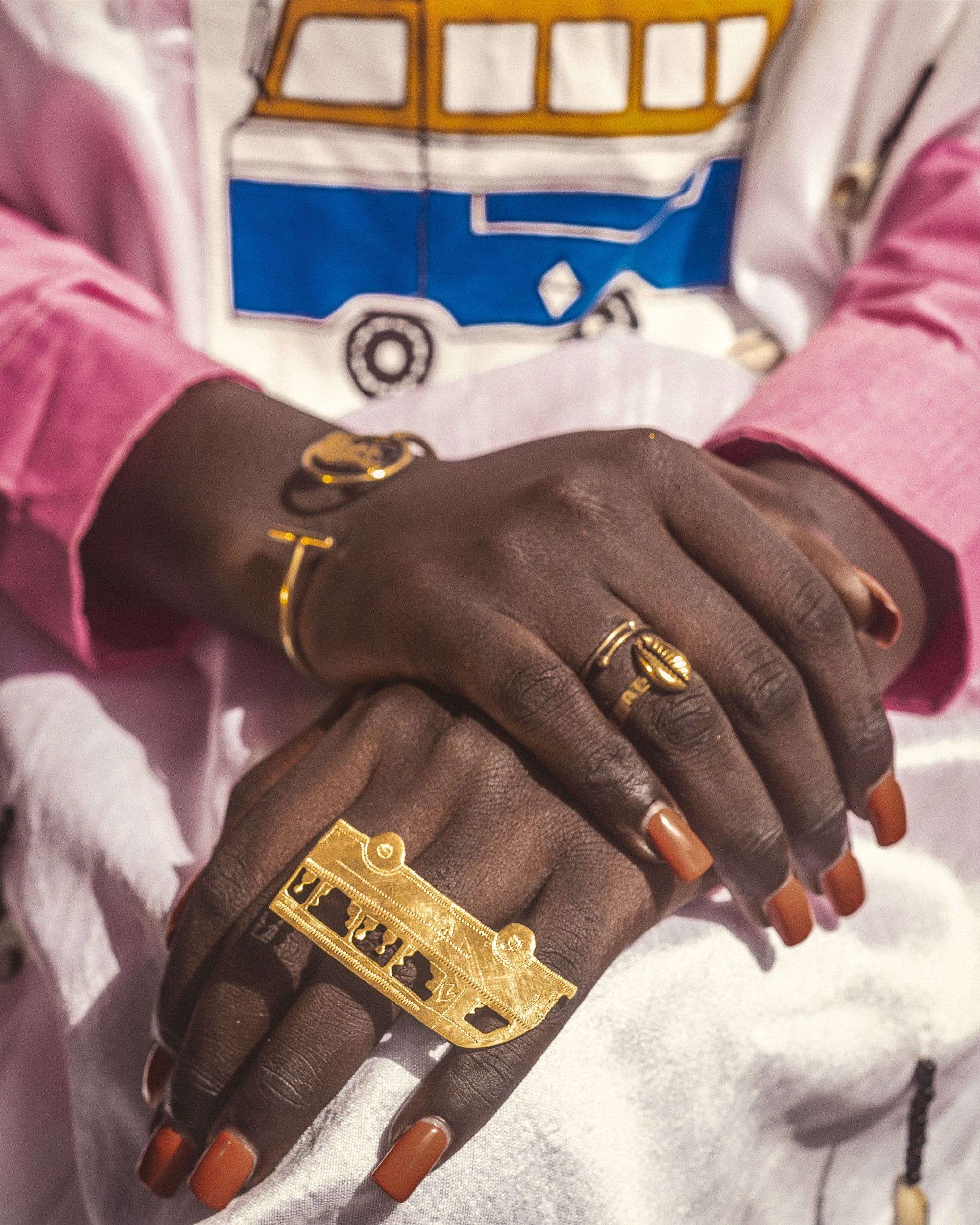 a portrait of two hands crossed on a lap while wearing gold rings, including one spanning several fingers of a bus