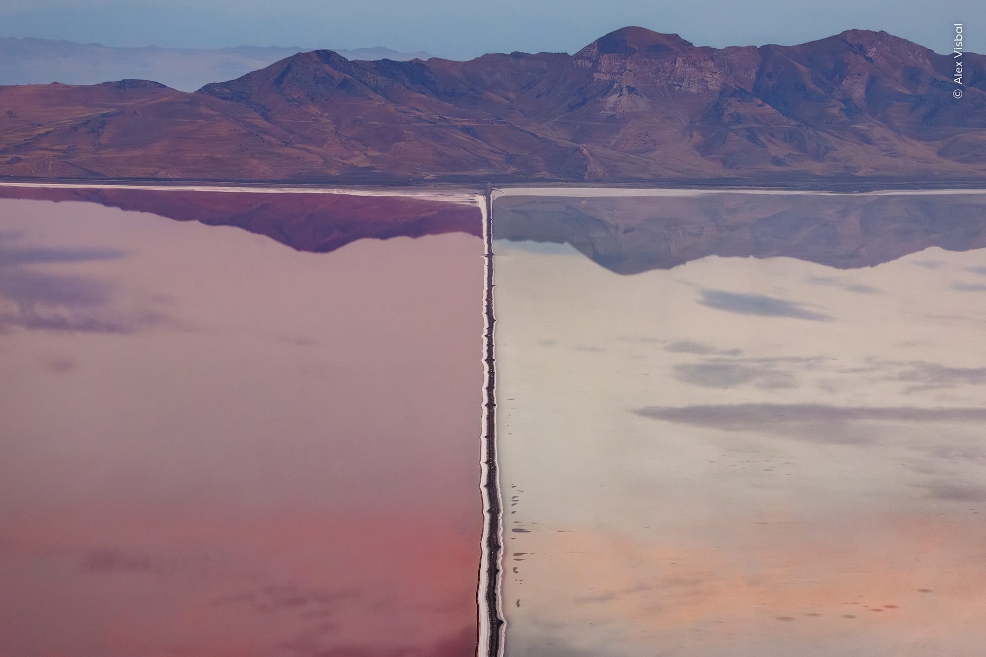 an aerial view of an engineered line trough a wetland with reflections of mountains that seem almost abstract